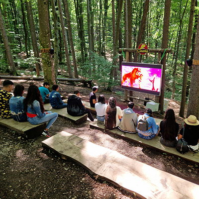 The children watch a documentary about dinosaurs on a screen in the forest